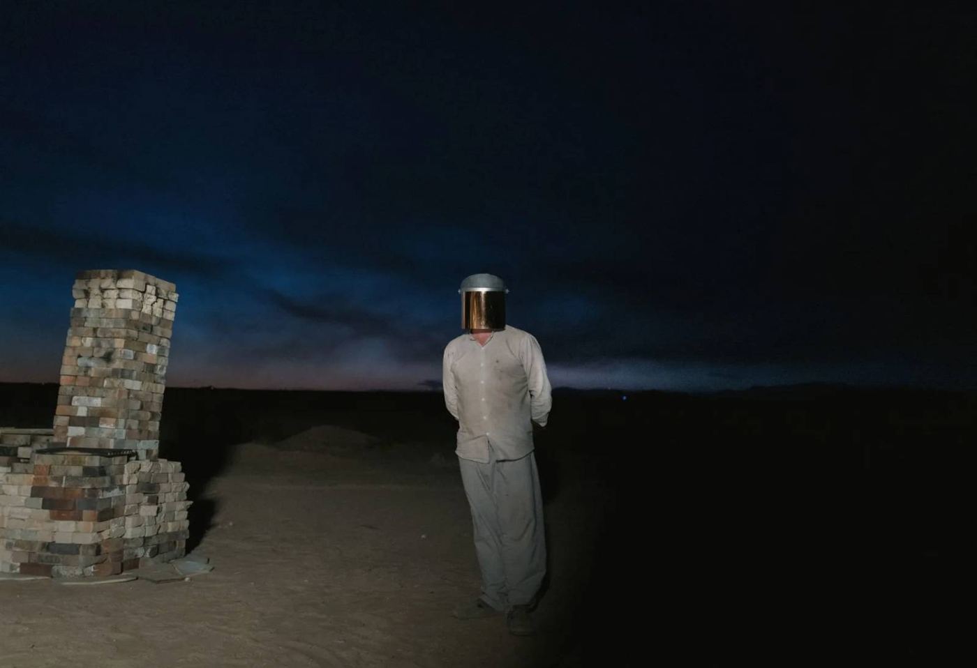 Figure in a white suit at dusk beside a stone pillar
